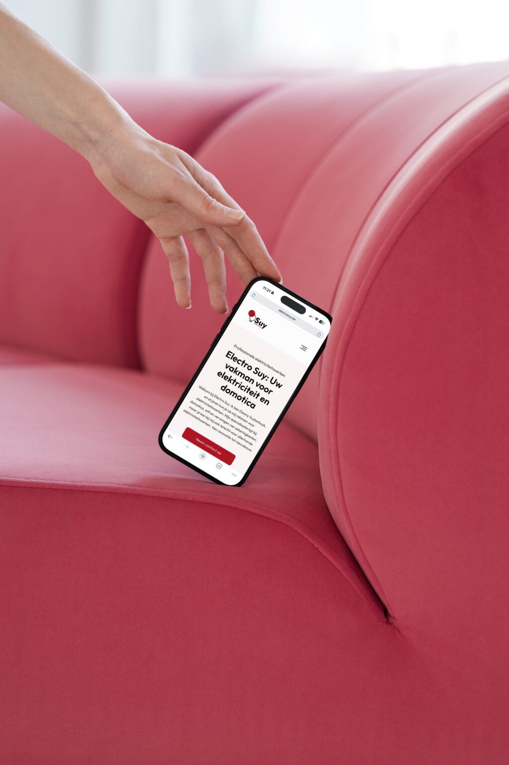 Hand houdt smartphone met Electro Suy website, op roze bank.
